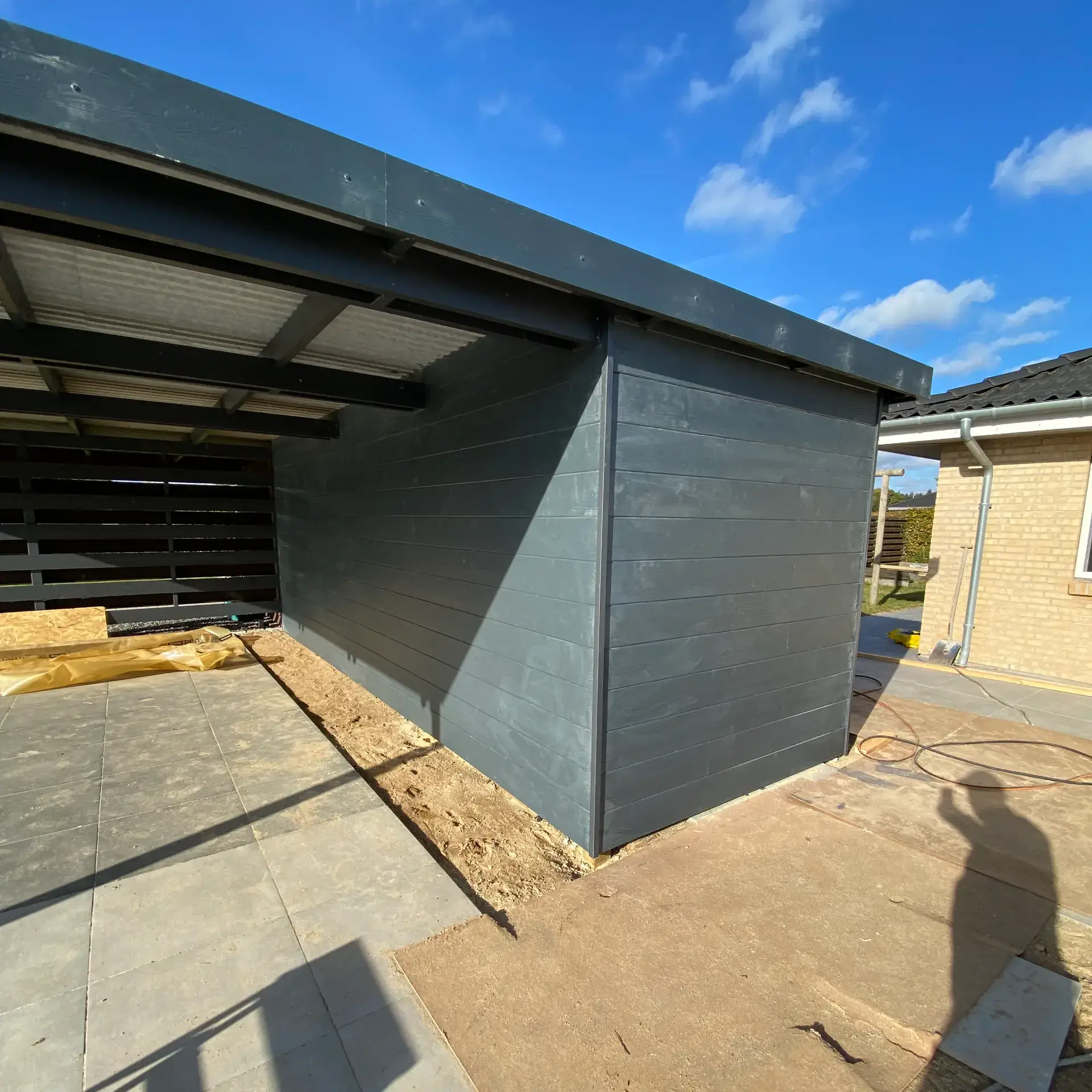 Udendørs husbygning under opførelse med sort facade og tag.