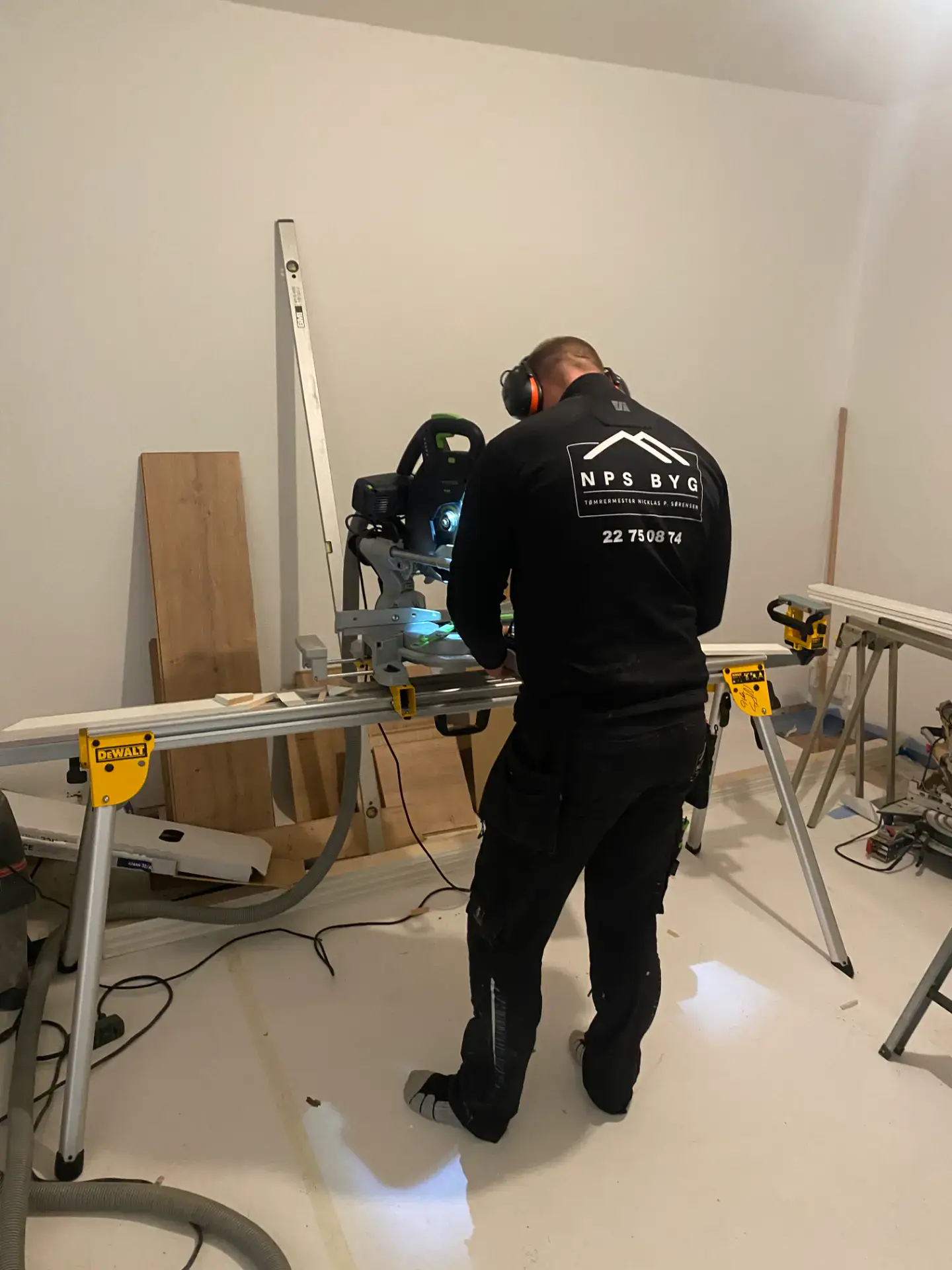 Mand arbejder med savskæring i byggeprojekt, sikkerhedsudstyr og værktøj.